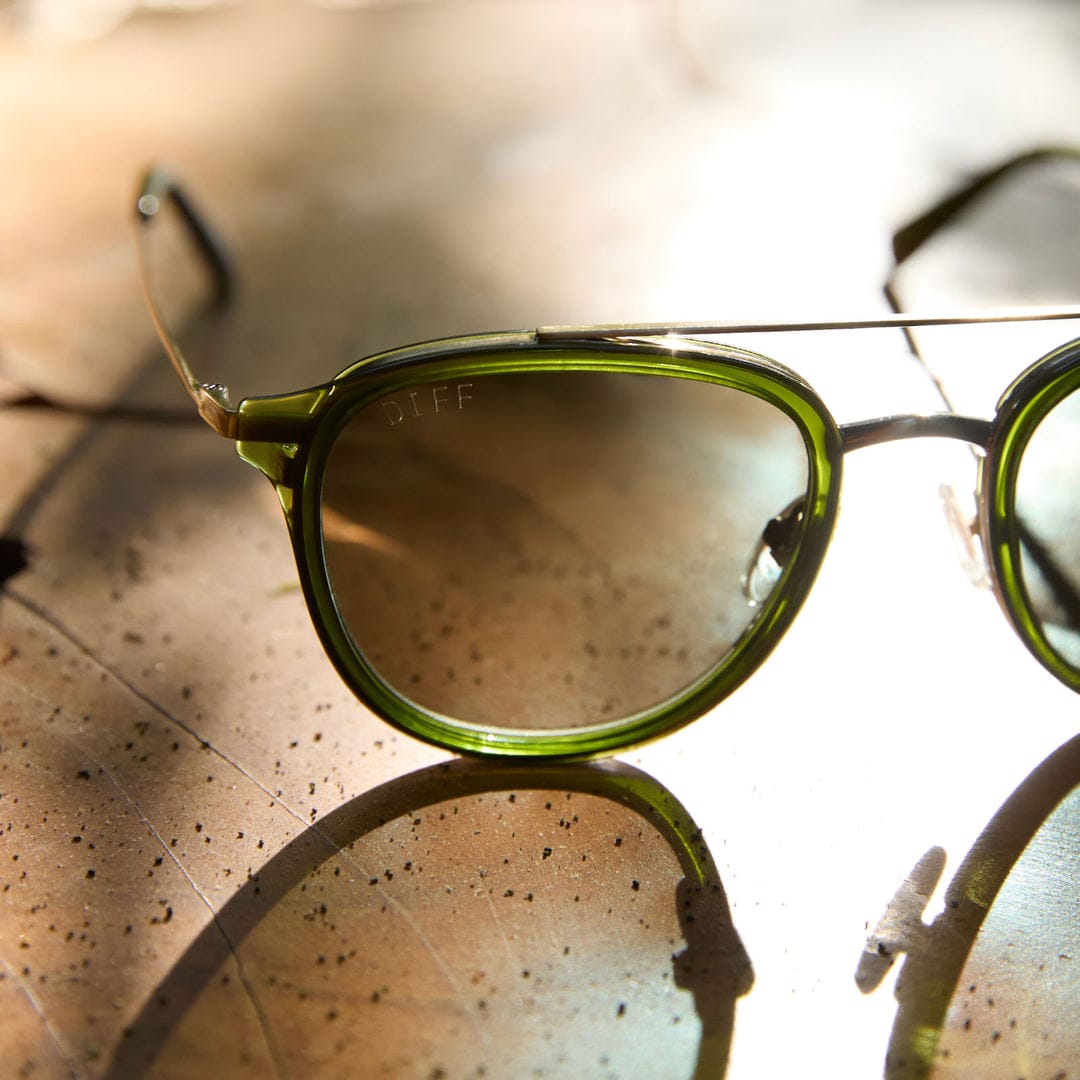 Close-up of Camden by DIFF polarized sunglasses in Olive, with translucent green frames and dark lenses on a sunlit surface.