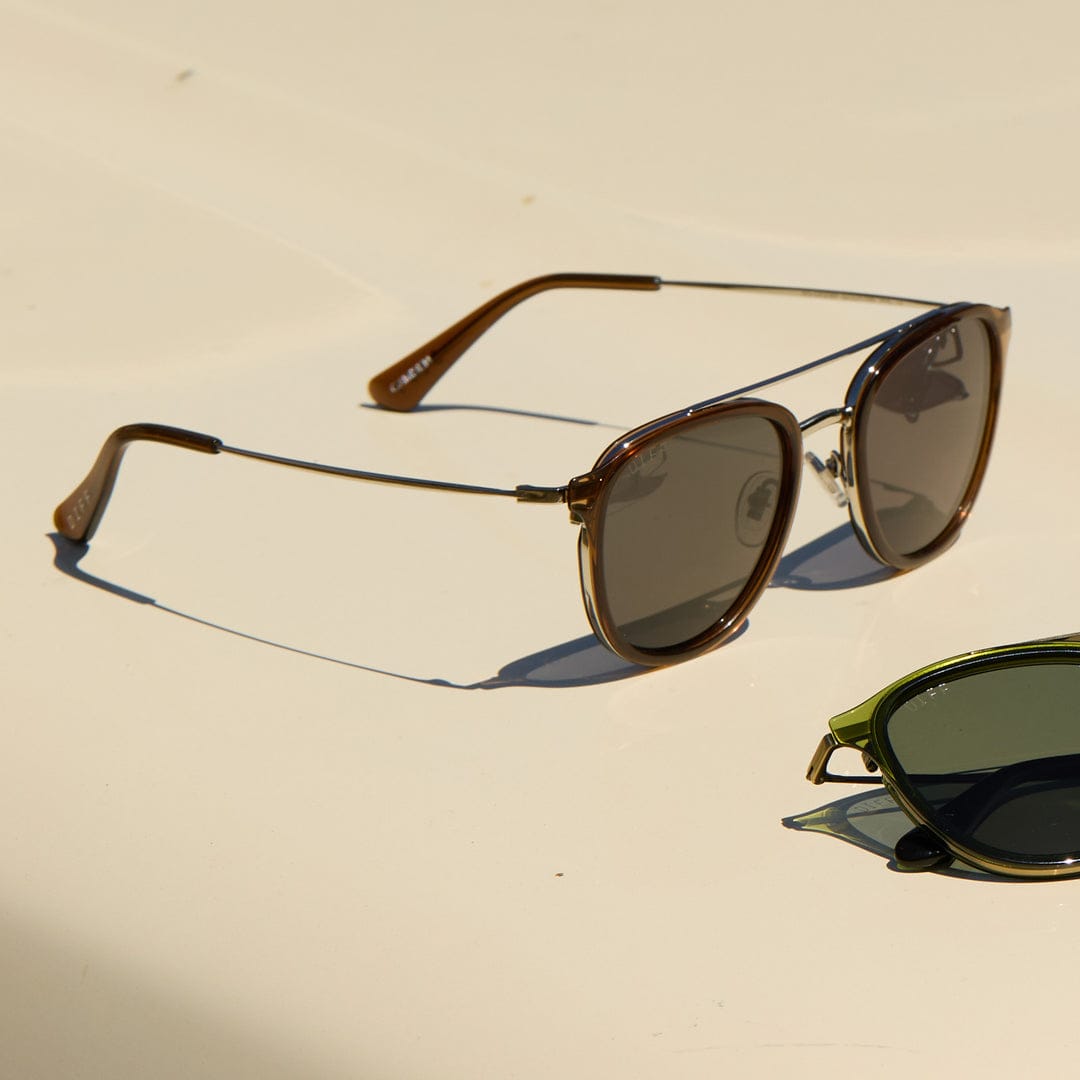Camden by DIFF polarized sunglasses in Whiskey, with brown frames and dark lenses, shown at an angle on a beige surface.
